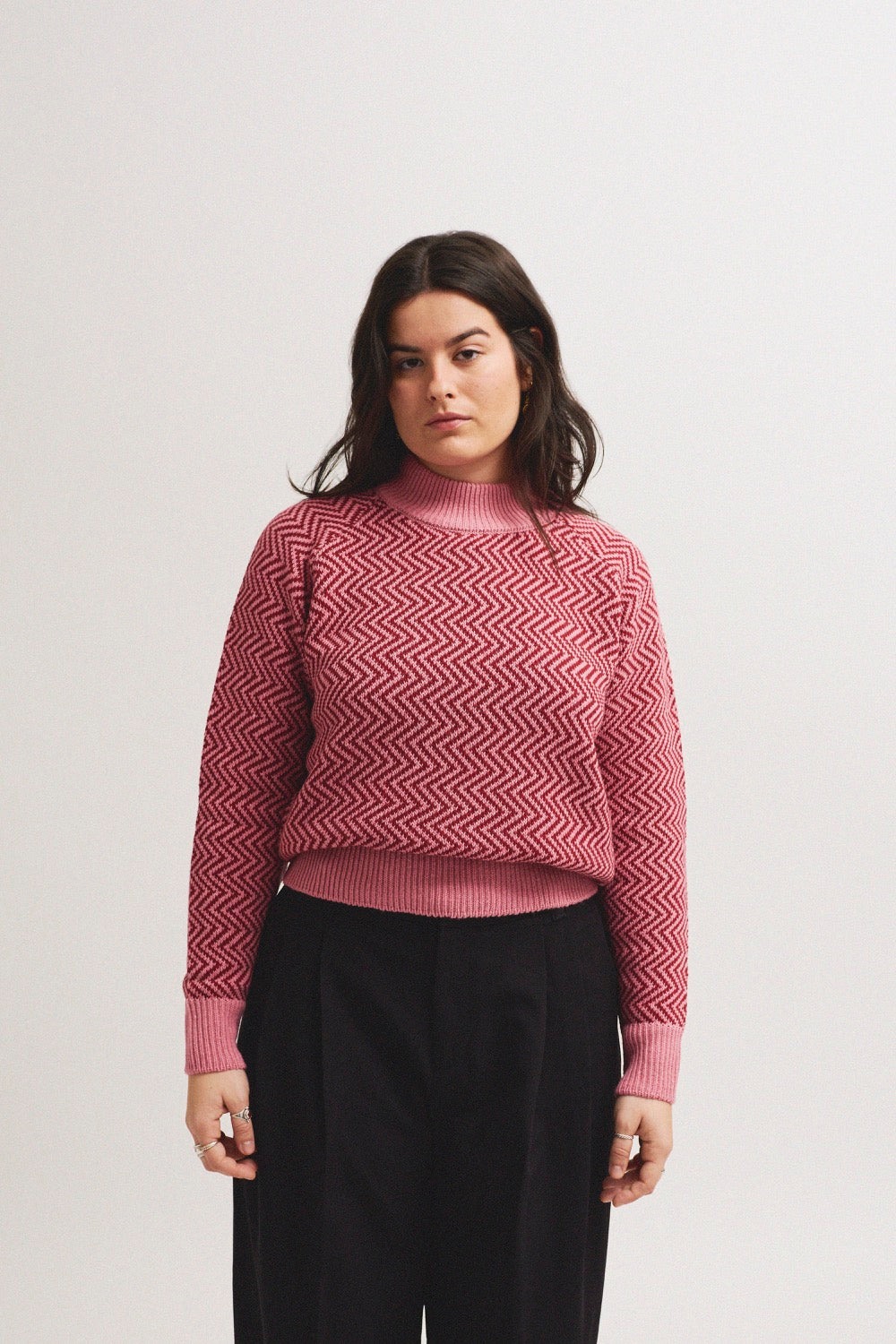 Modelo con jersey de mujer IAIOS rosa con patrón zigzag en tonos burdeos y cuello alto, hecho en Catalunya (España) con hilo reciclado.