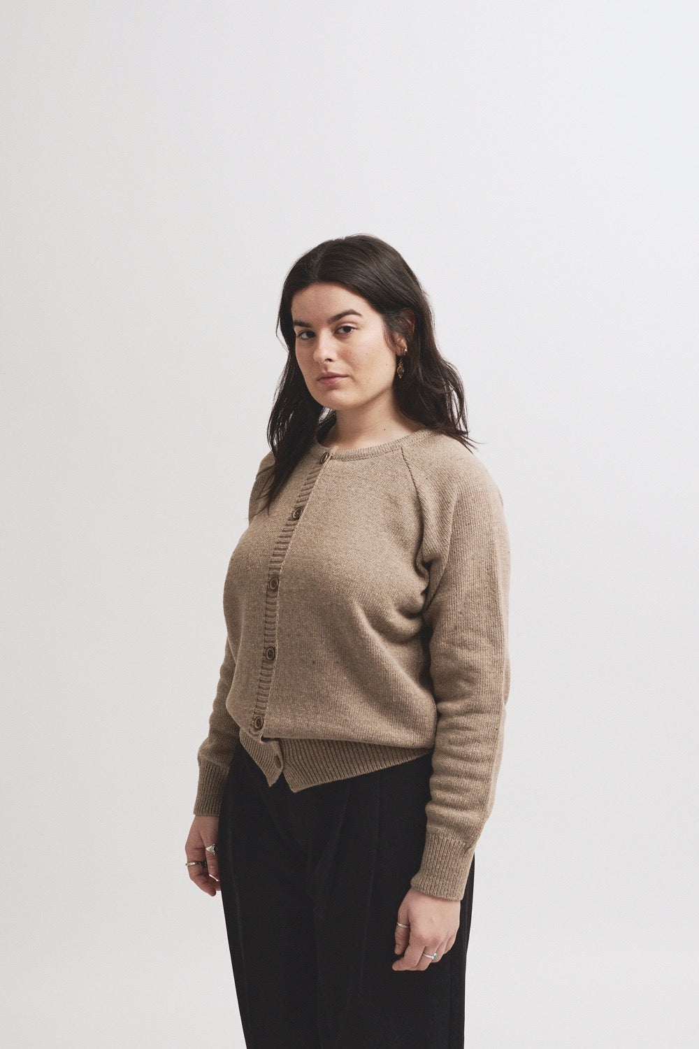 Modelo con cardigan IAIOS de punto beige o marrón claro con botones frontales, manga larga y terminaciones acanaladas, hecho en Catalunya (España) con hilo reciclado.