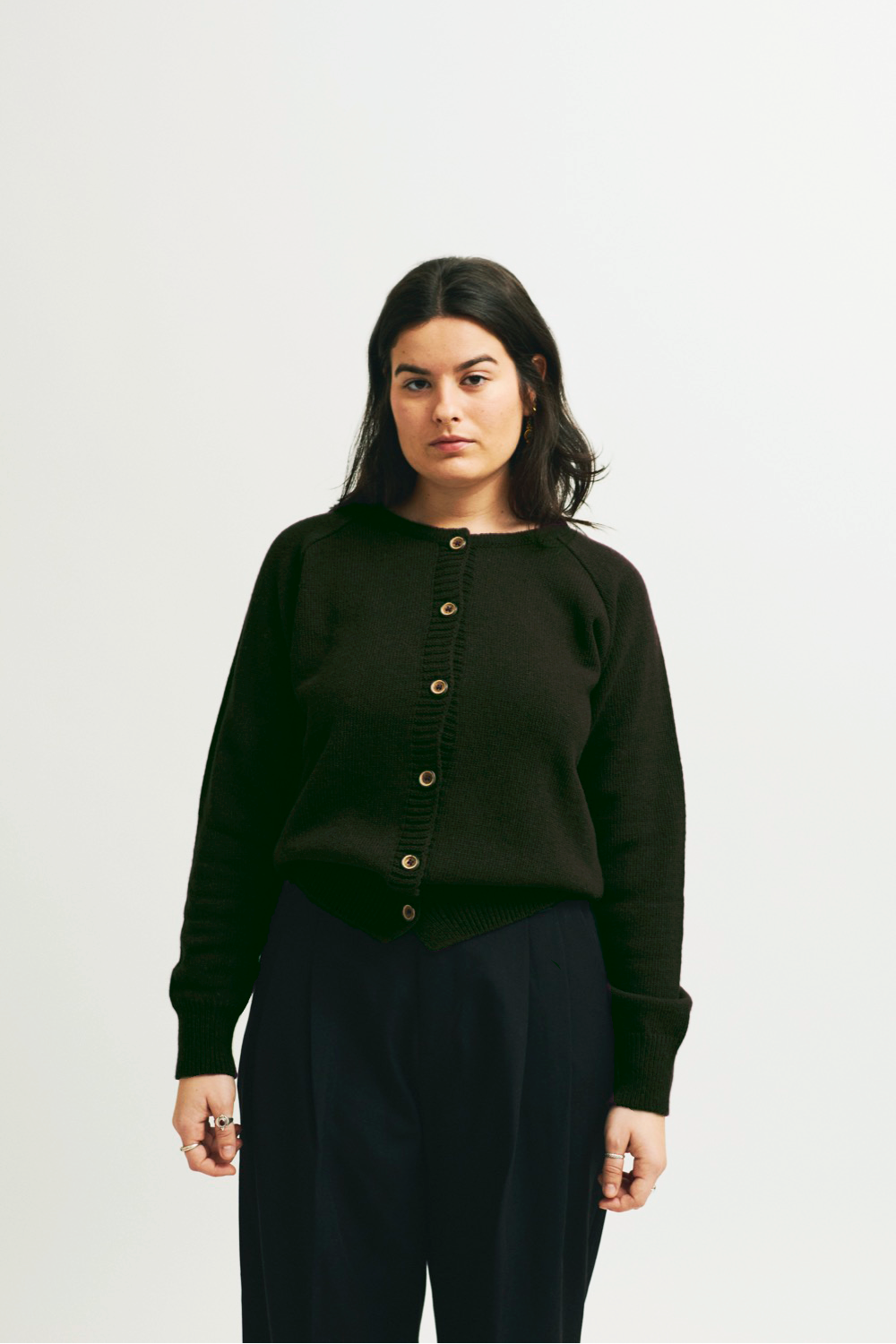Modelo con cardigan IAIOS de punto verde oscuro con botones frontales, manga larga y terminaciones acanaladas, hecho en Catalunya (España) con hilo reciclado.