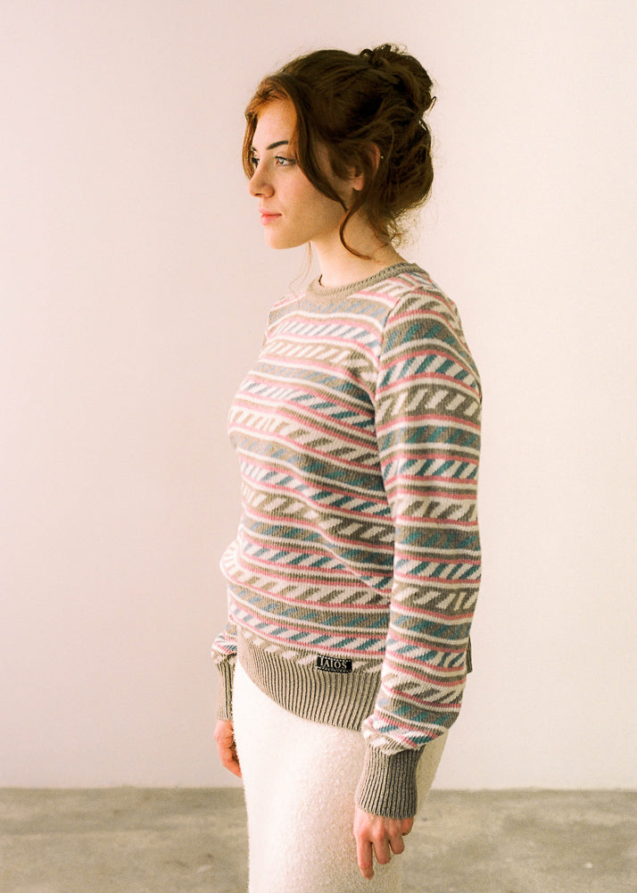 La modelo lleva el jersey de mujer IAIOS en color beige con detalles en rosa, azul y blanco, hecho en Catalunya (España) con hilo reciclado, ideal para invierno.