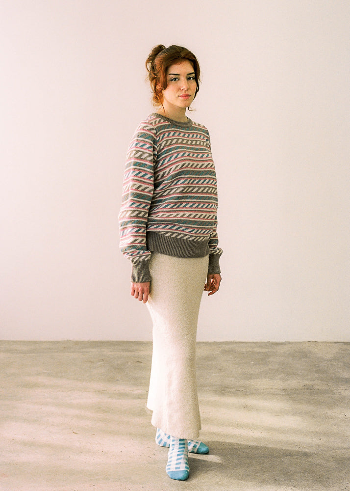 La modelo lleva el jersey IAIOS de mujer beige con delicados detalles en rosa, azul y blanco, moda sostenible elaborada en talleres de Catalunya (España) con hilo reciclado.