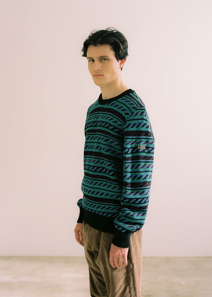 Jersey puesto en modelo, visión lateral en la que se puede apreciar la etiqueta con logo en la manga. El modelo lleva el jersey unisex IAIOS con cenefa en tonos azul, verde y negro, moda sostenible hecha en Catalunya (España) con hilo reciclado, ideal para invierno.