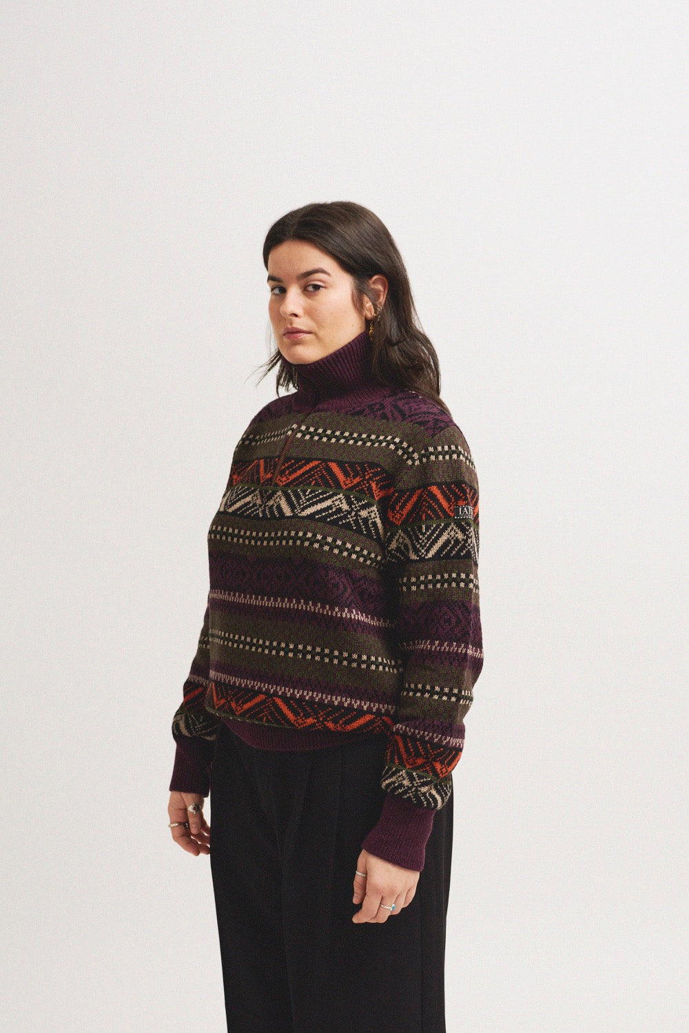 El modelo lleva el jersey unisex IAIOS azul oscuro con cuello alto y cremallera completa, ajuste relajado, hecho en Catalunya (España) con hilo reciclado.