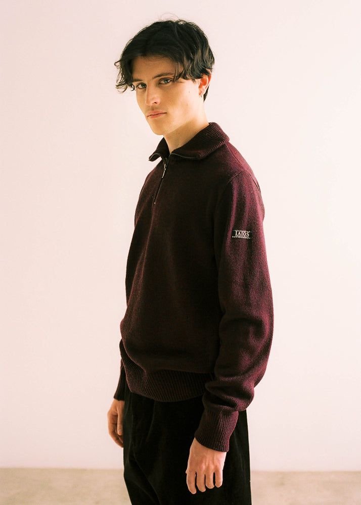 El modelo lleva el jersey unisex IAIOS granate con media cremallera, moda sostenible hecha en Catalunya (España) con hilo reciclado, básico atemporal ideal para invierno.