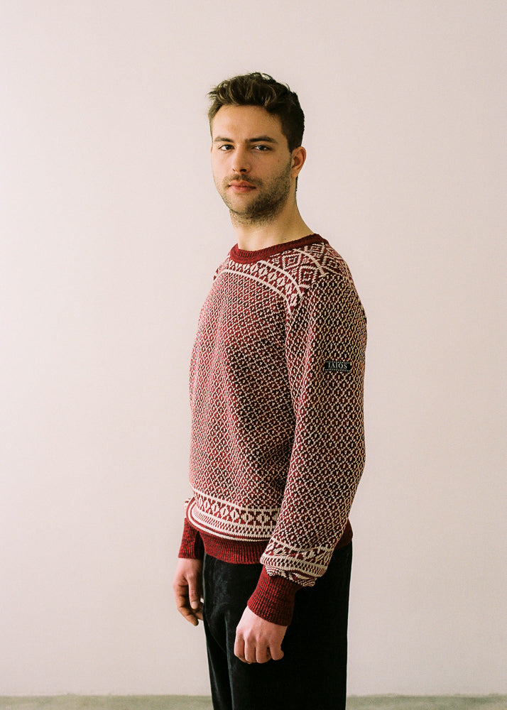 El modelo lleva el jersey de hombre IAIOS rojo y blanco con diseño jacquard navideño tipo nórdico, moda sostenible hecha en Catalunya (España) con hilo reciclado, ideal para invierno.