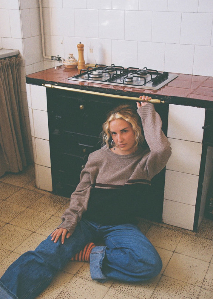 La modelo lleva el jersey unisex IAIOS negro y marrón claro con raya granate, inspirado en los años 90, moda sostenible hecha en Catalunya (España) con hilo reciclado.