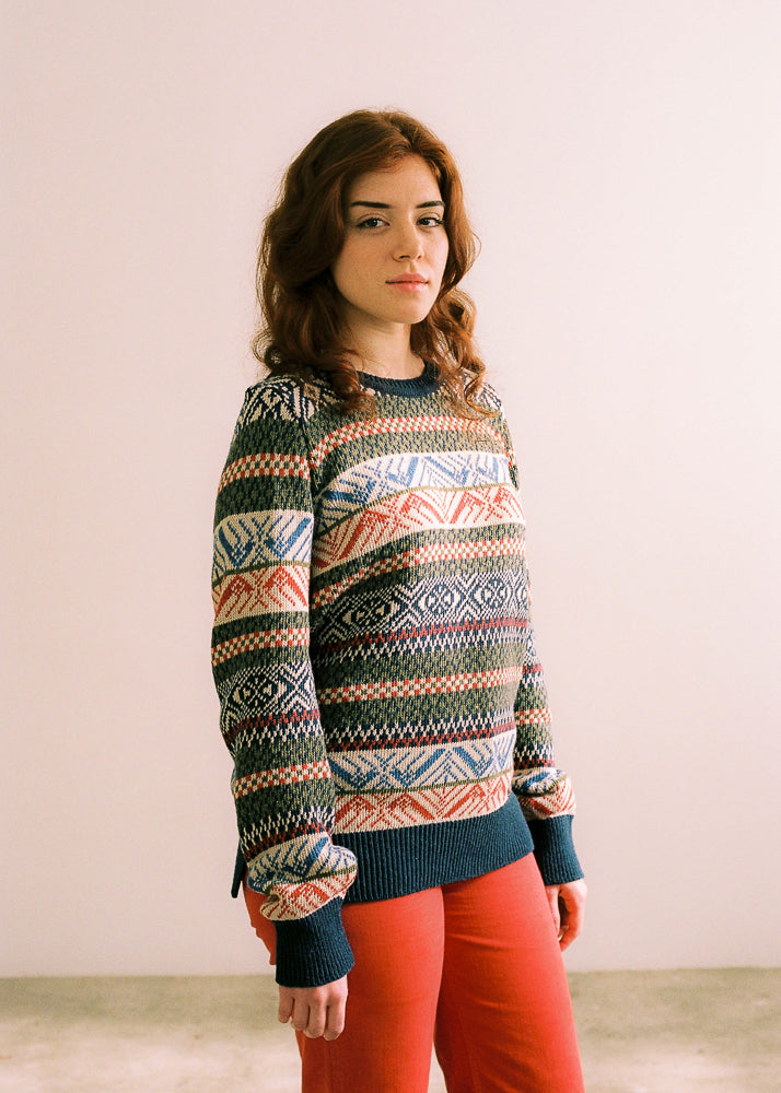 La modelo lleva el jersey de mujer IAIOS con motivos invernales tipo nórdico en colores azul marino, blanco y rojo, moda sostenible hecha en Catalunya (España) con hilo reciclado.