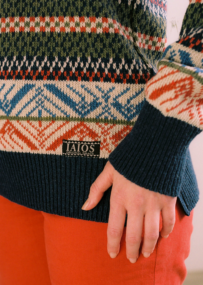 Fotografía de detalle del jersey, se aprecia la etiqueta con logo en lel bajo y los colores y motivos del tejido. Jersey de mujer IAIOS tipo nórdico en tonos marineros, detalle del tejido con motivos invernales, moda sostenible elaborada con hilo reciclado en talleres de Catalunya (España).