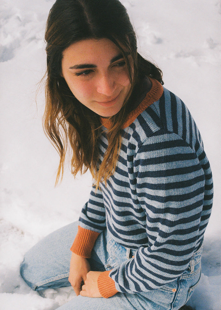 La modelo lleva el jersey unisex IAIOS de rayas azules y naranja, moda sostenible hecha en Catalunya (España) con hilo reciclado, ideal para invierno.