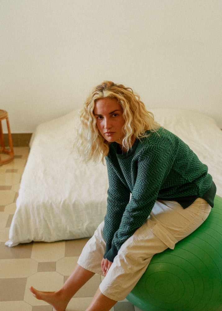 La modelo lleva el jersey unisex IAIOS verde con diseño de zigzag, moda sostenible hecha en Catalunya (España) con hilo reciclado, ideal para invierno.