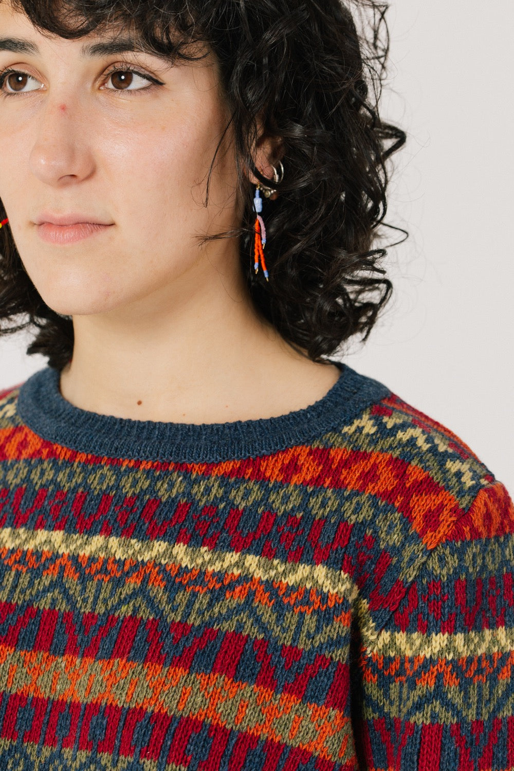 Detalle de la modelo con el jersey. La modelo lleva el jersey unisex IAIOS colorido de inspiración navideña en tonos rojos, naranjas y azules, moda sostenible hecha en Catalunya (España) con hilo reciclado.