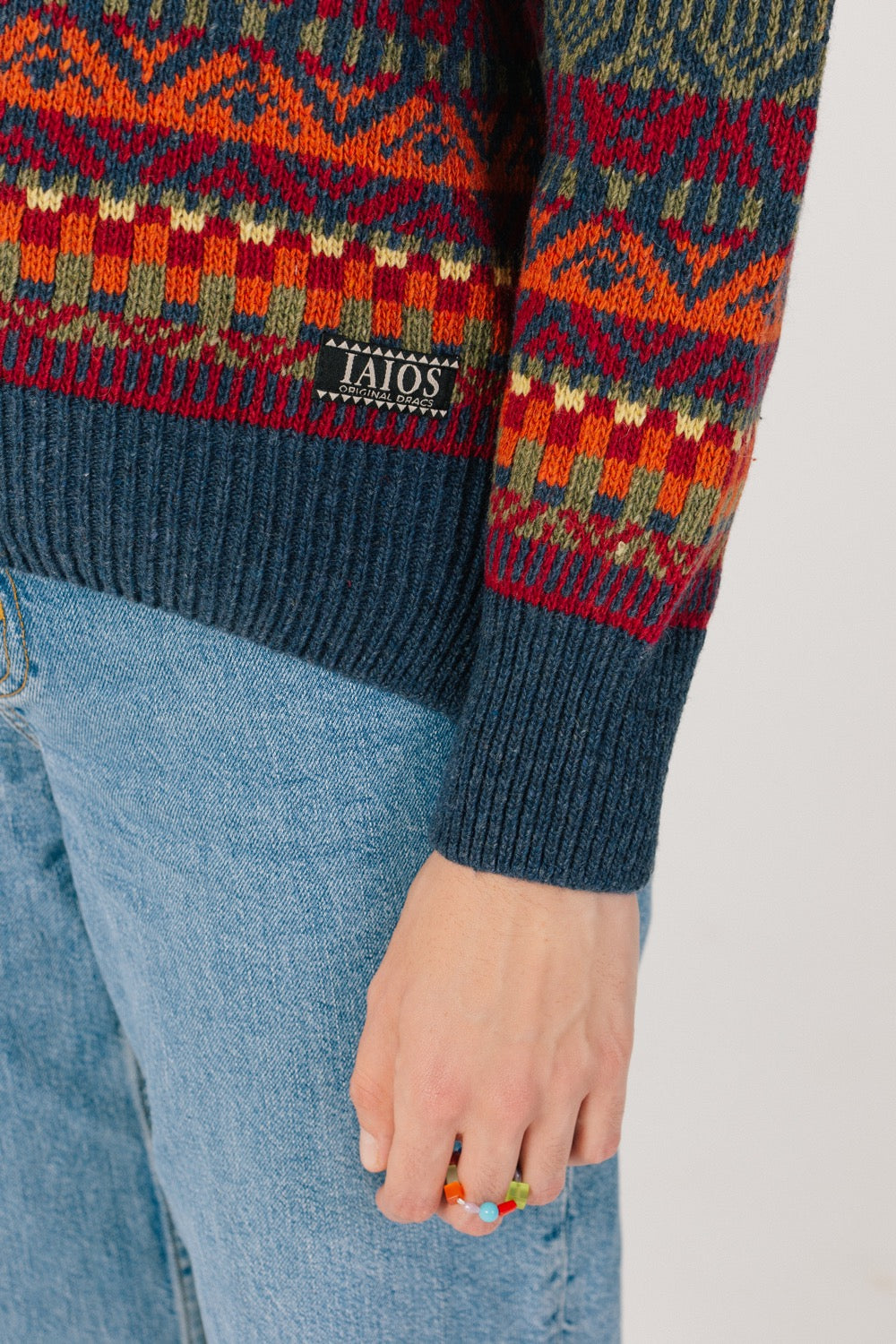 Detalle del bajo del jersey donde podemos ver la etiqueta de iaios. Jersey unisex IAIOS colorido navideño, detalle del tejido, moda sostenible elaborada con hilo reciclado en talleres de Catalunya (España).