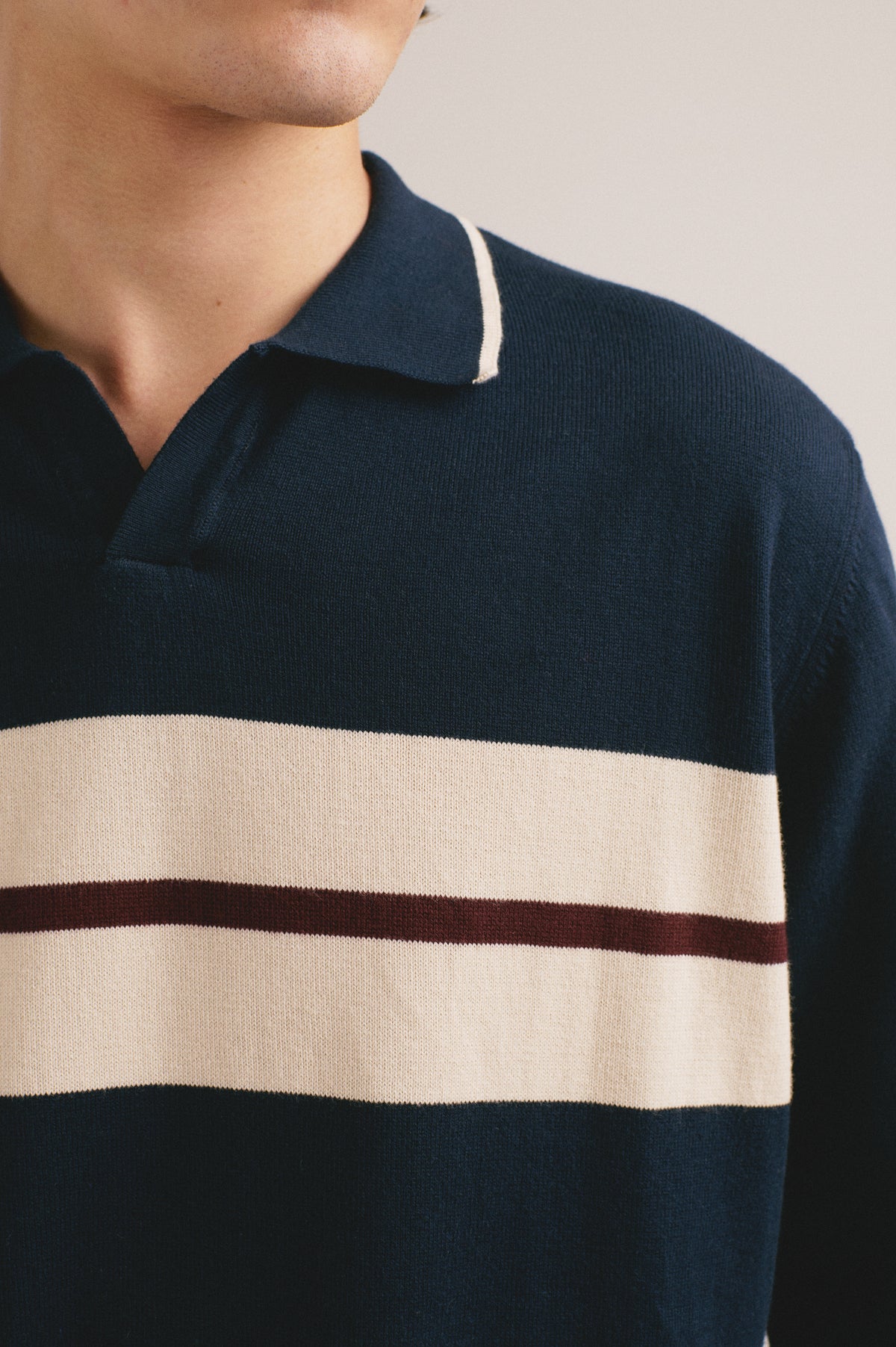 Detalle del polo azul marino con una franja en el pecho color beige y una linea rojo
