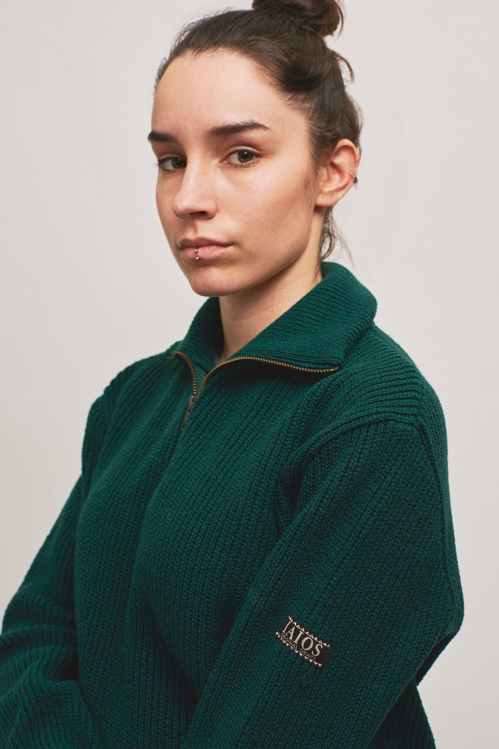 Modelo con jersey unisex IAIOS acanalado en punto inglés color verde botella oscuro con media cremallera, hecho en Catalunya (España) con hilo reciclado.