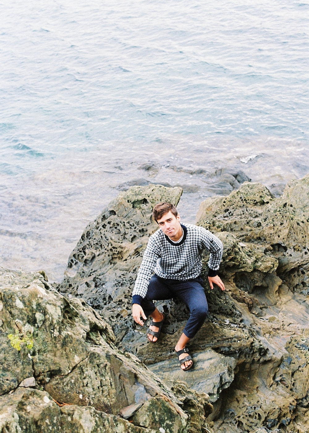 Photograph of the sweater in a seated model and paired with navy blue pants.