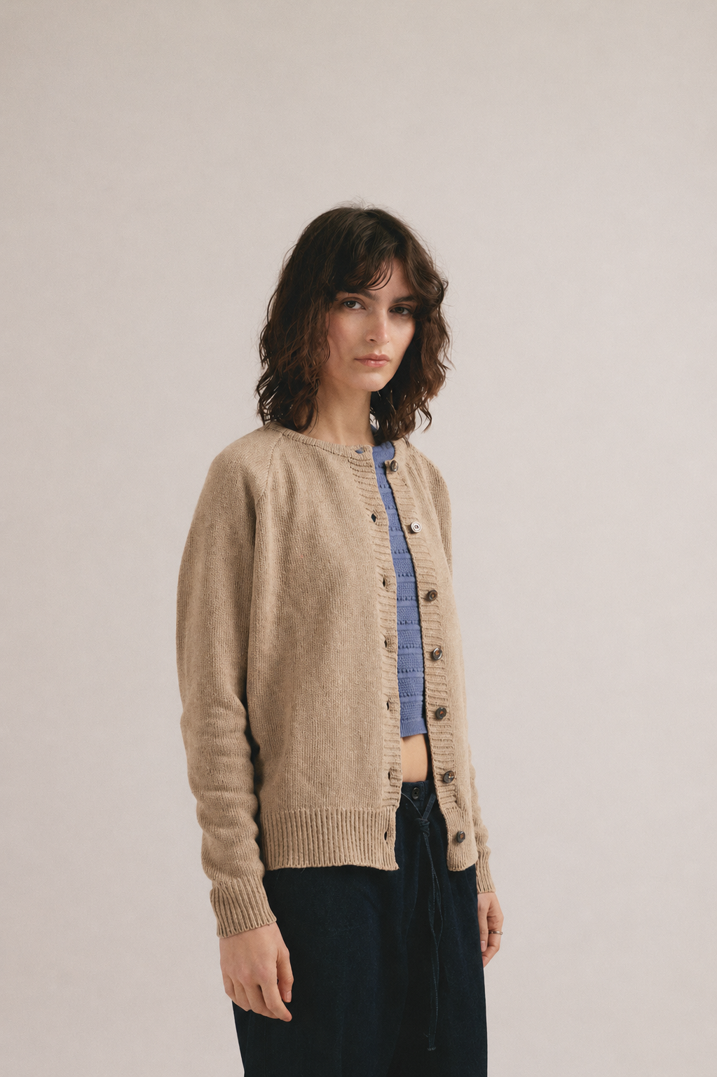 Mujer joven vistiendo cárdigan beige de punto abierto con botones y look casual minimalista.