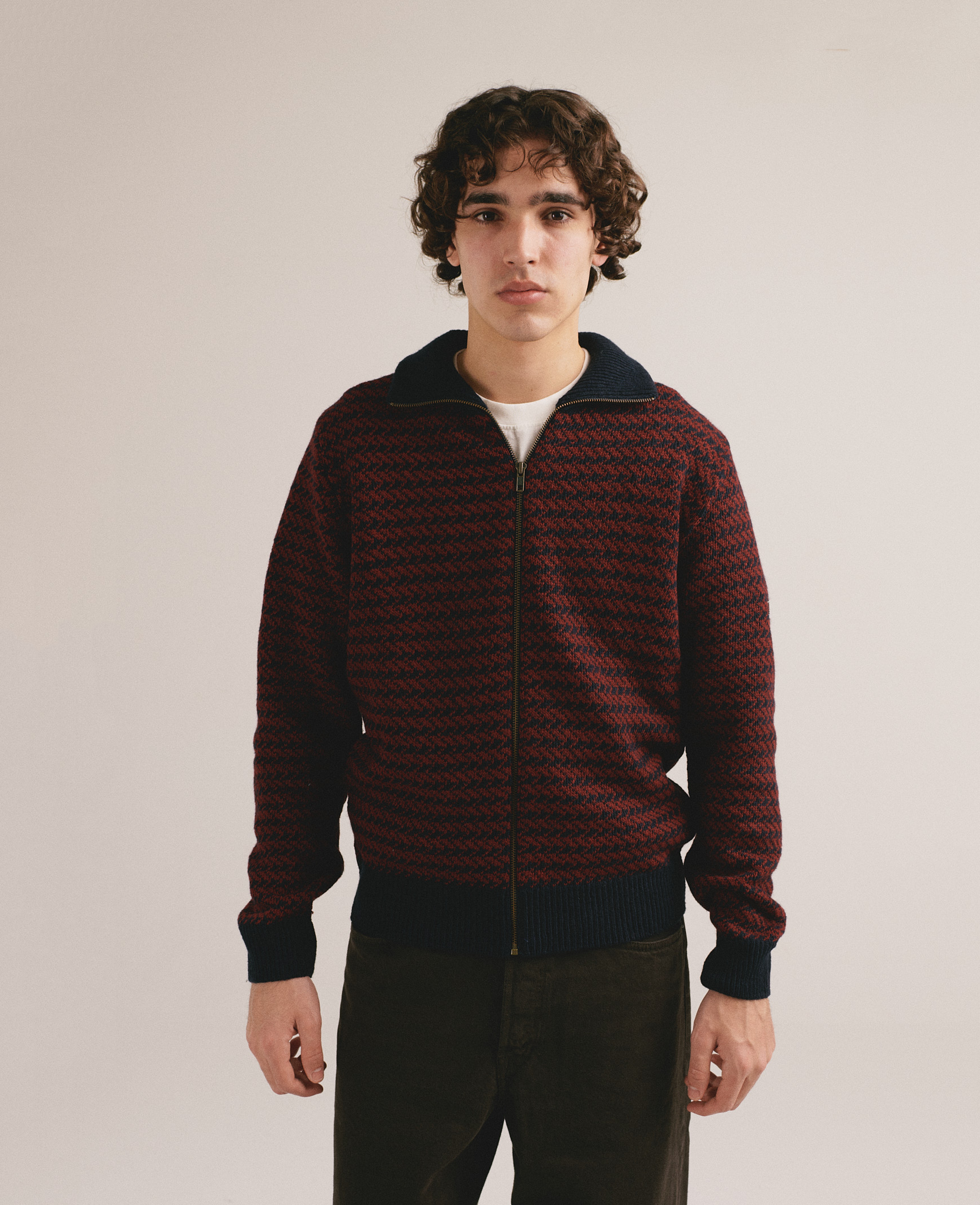 Hombre con cárdigan de punto rojo y negro con cremallera de IAIOS y pantalón oscuro.