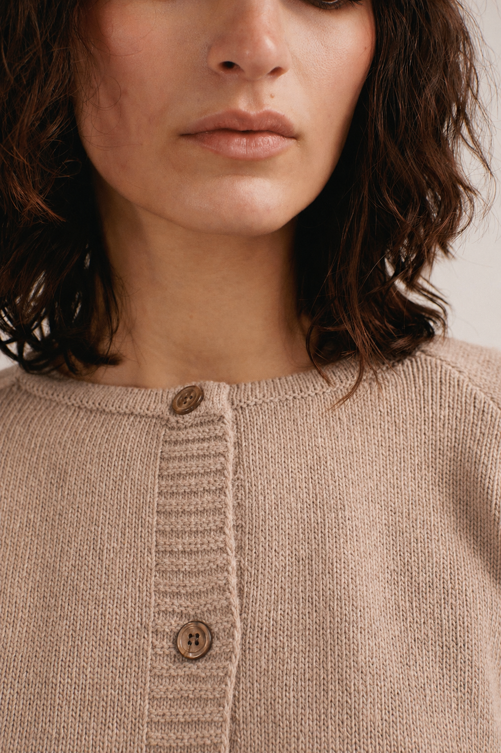 Mujer con cárdigan de punto beige con botones de IAIOS sobre camiseta azul y pantalón oscuro.