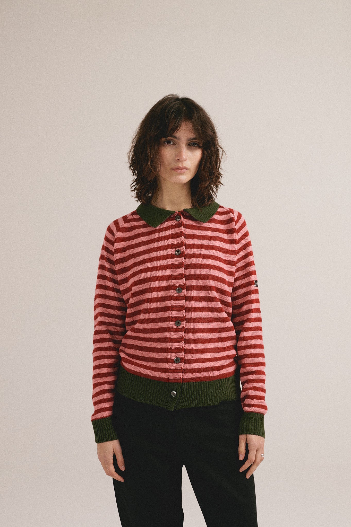 Mujer con cárdigan de punto a rayas rojas y rosas con cuello verde de IAIOS y pantalón oscuro.
