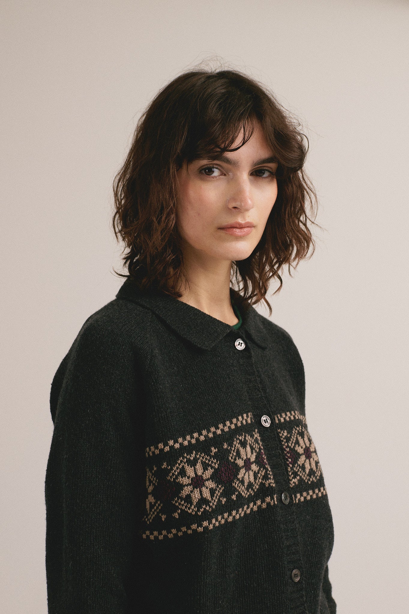 Mujer joven vistiendo cárdigan negro de punto con patrón decorativo en el pecho y estilo casual.