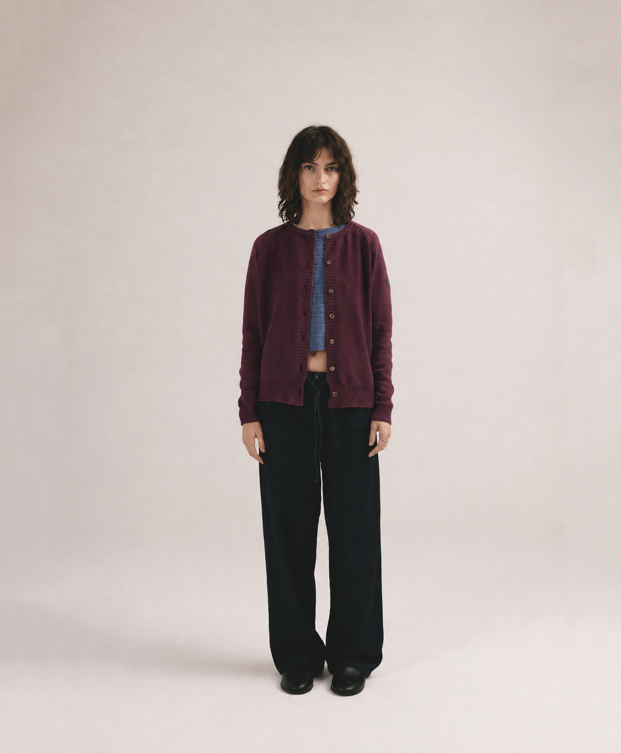 Mujer con cárdigan de punto morado con botones de IAIOS y pantalón oscuro en fondo neutro.
