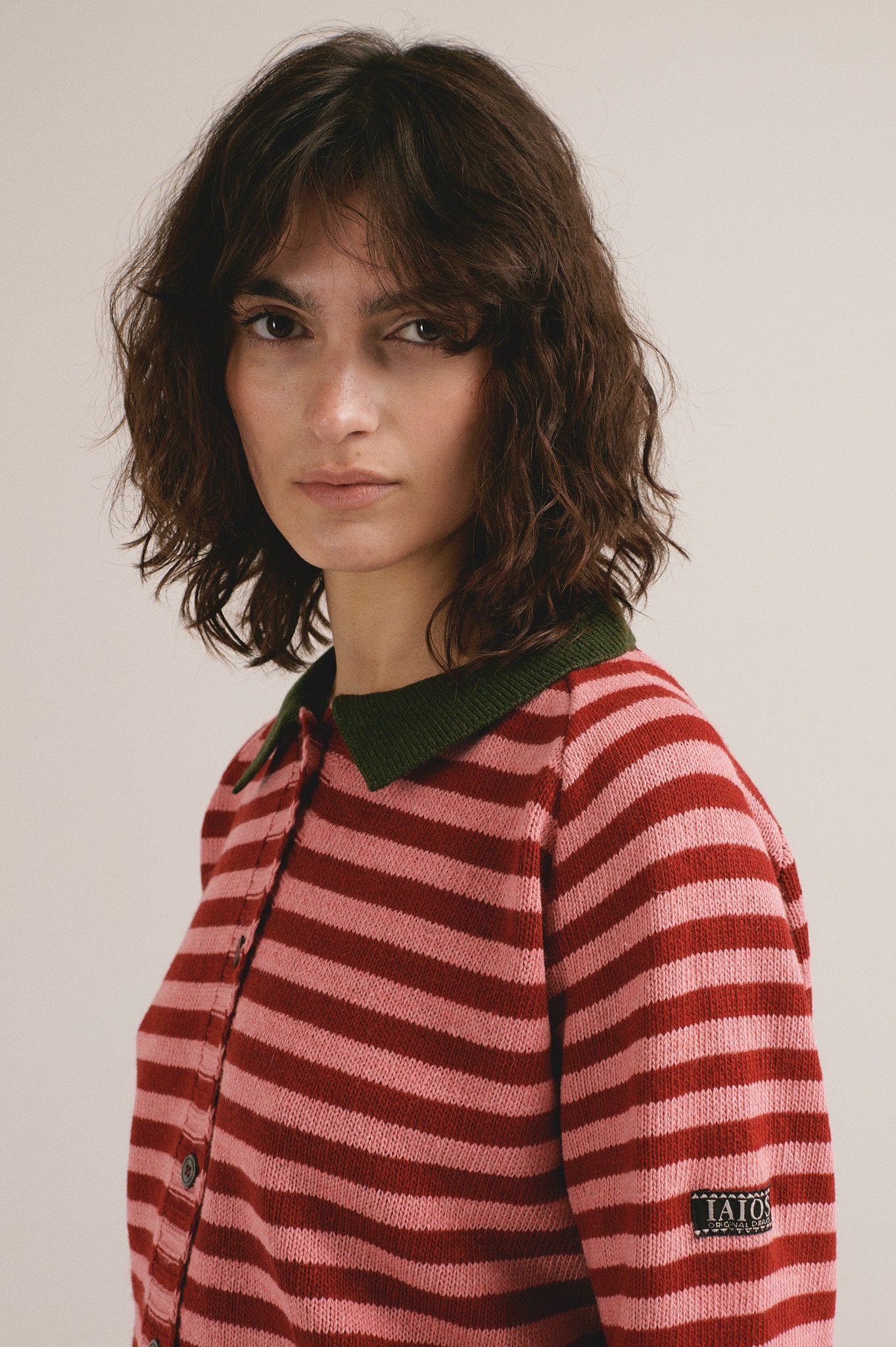 Modelo femenina con chaqueta de punto de rayas en tonos rojos con botones y cuello verde de IAIOS.