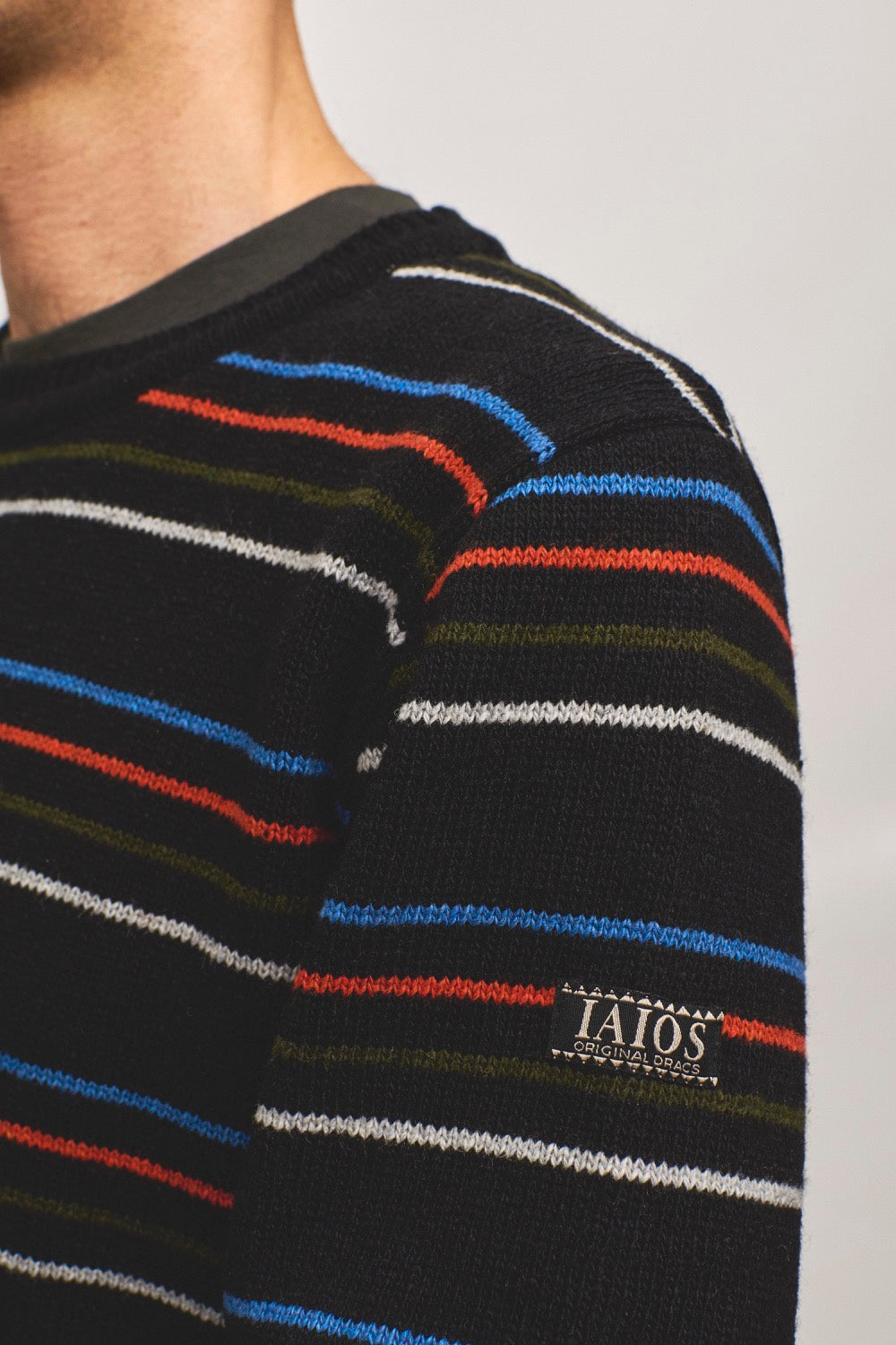 Detalle del tejido del jersey unisex negro con rayas finas en tonos vivos, hecho con hilo reciclado en talleres de Catalunya (España), moda sostenible y duradera.