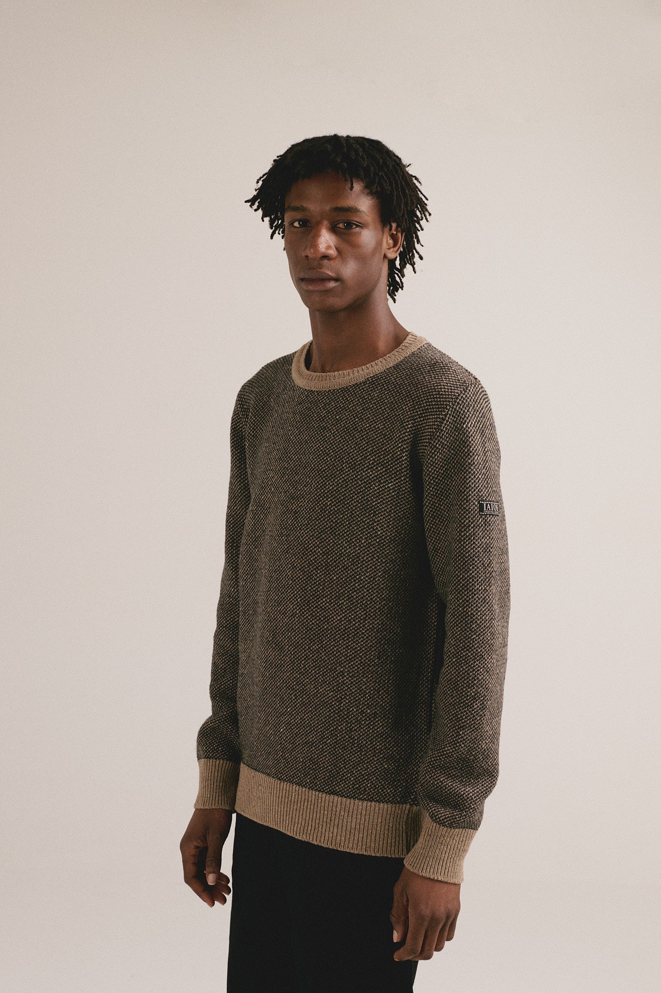 Hombre con jersey de punto marrón bicolor y pantalón oscuro en look completo