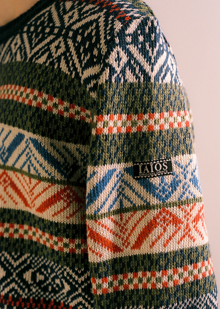 Fotografía de detalle donde se ve la etiqueta del logo de  IAIOS en la manga del jersey. Jersey de hombre IAIOS tipo nórdico azul marino, detalle del tejido con motivos invernales, moda sostenible elaborada con hilo reciclado en talleres de Catalunya (España).