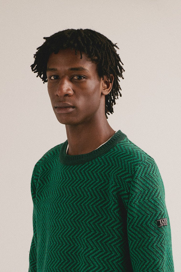 Hombre con jersey de punto verde con estampado geométrico de IAIOS y pantalón oscuro.