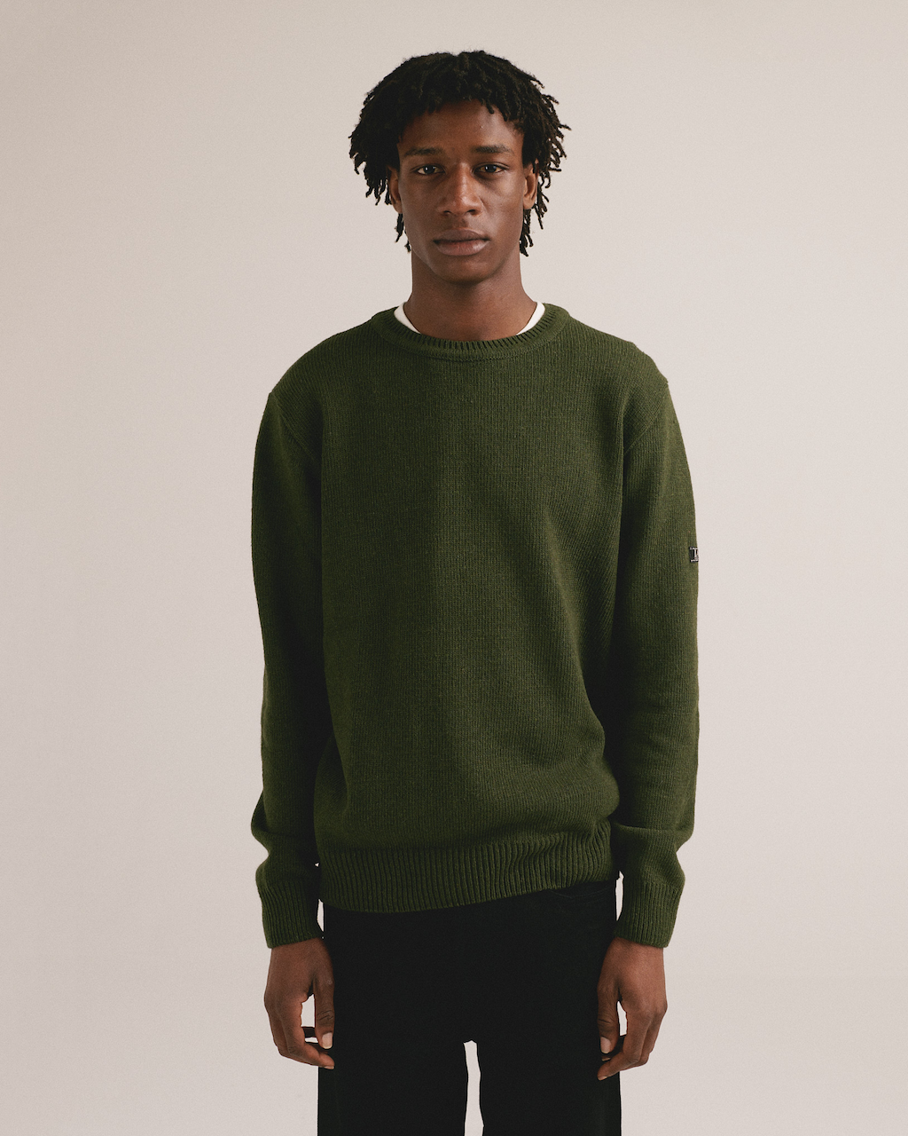 Hombre con jersey de punto verde liso de IAIOS y pantalón oscuro en fondo neutro.