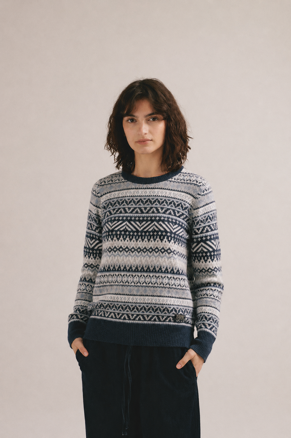 Mujer joven vistiendo jersey de punto con patrón geométrico en gris y azul y estilo casual de invierno.