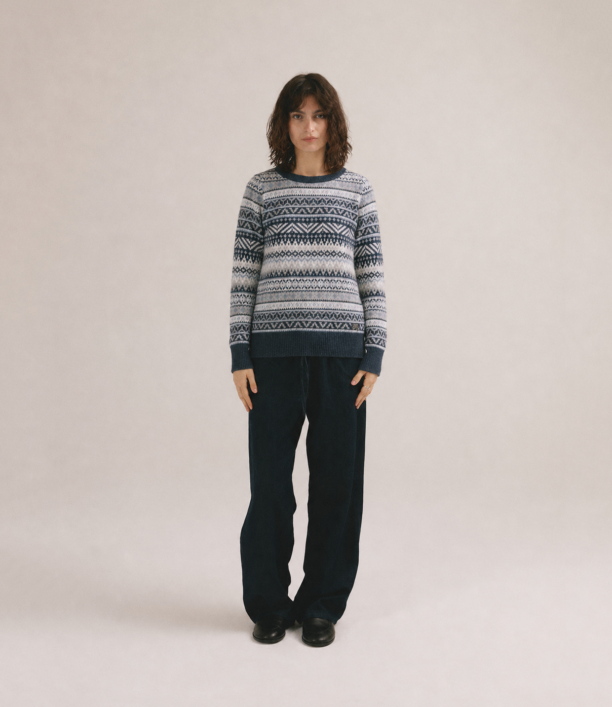 Mujer con jersey de punto gris y azul con estampado geométrico de IAIOS y pantalón oscuro.