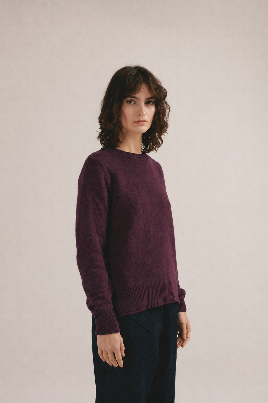 Mujer con jersey de punto morado liso de IAIOS y pantalón oscuro en fondo neutro.