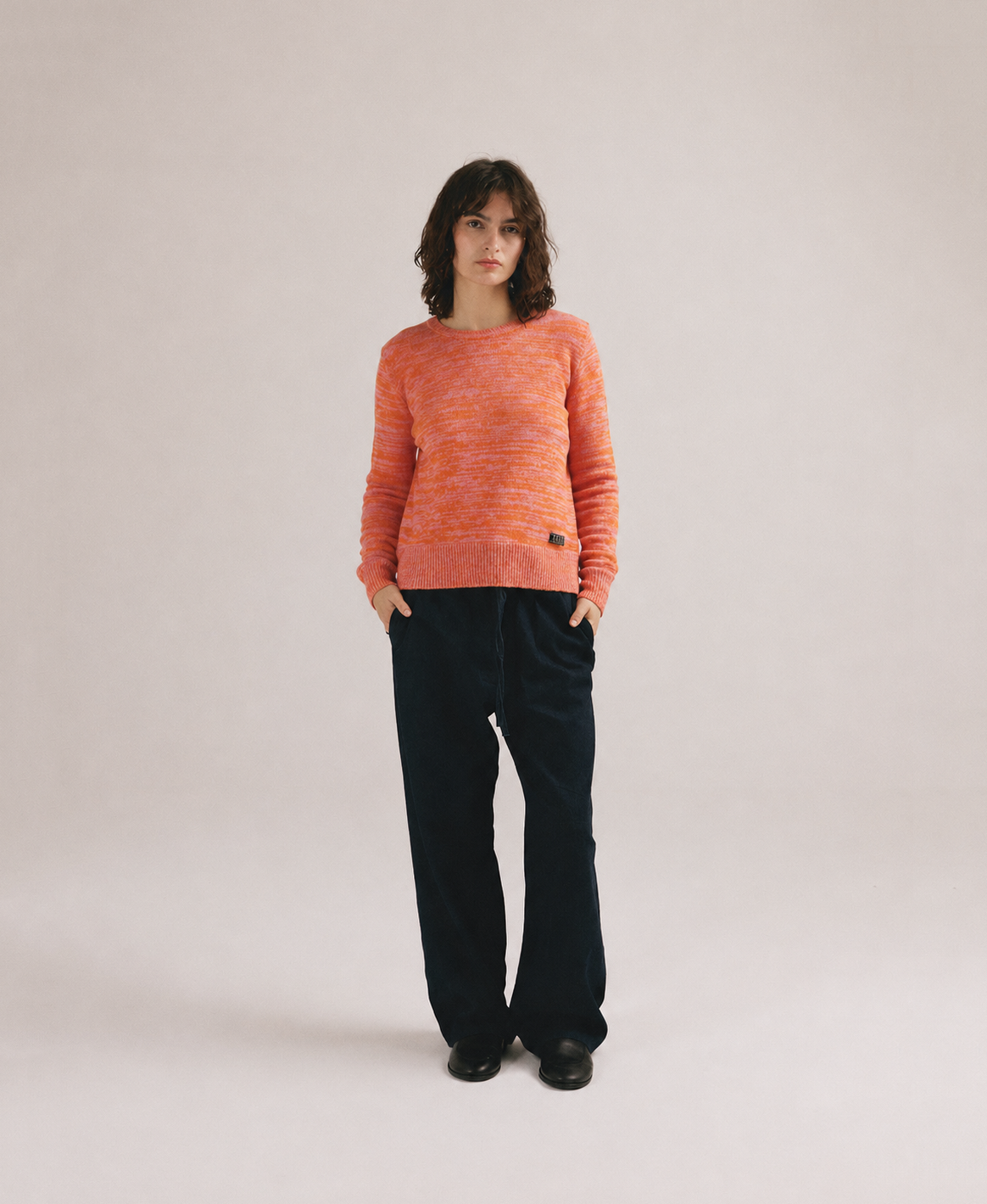 Mujer con jersey de punto naranja jaspeado de IAIOS y pantalón oscuro en fondo neutro.