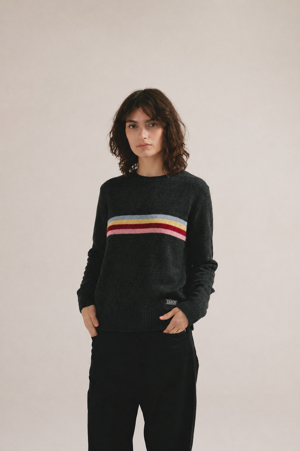 Mujer joven vistiendo jersey negro de punto con franja horizontal de colores y estilo casual moderno.