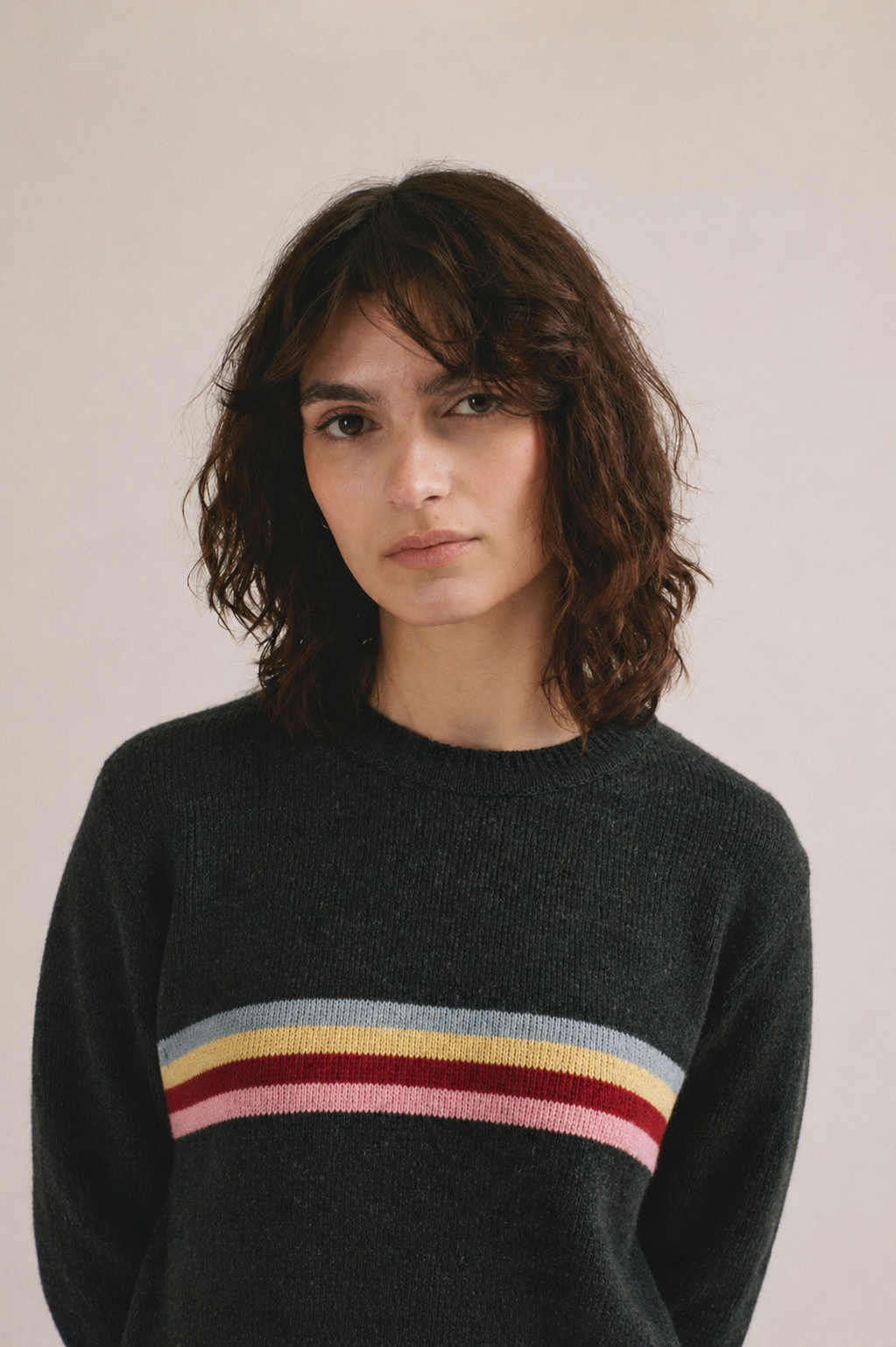 Mujer con jersey de punto negro con franja multicolor en el pecho de IAIOS y pantalón oscuro.