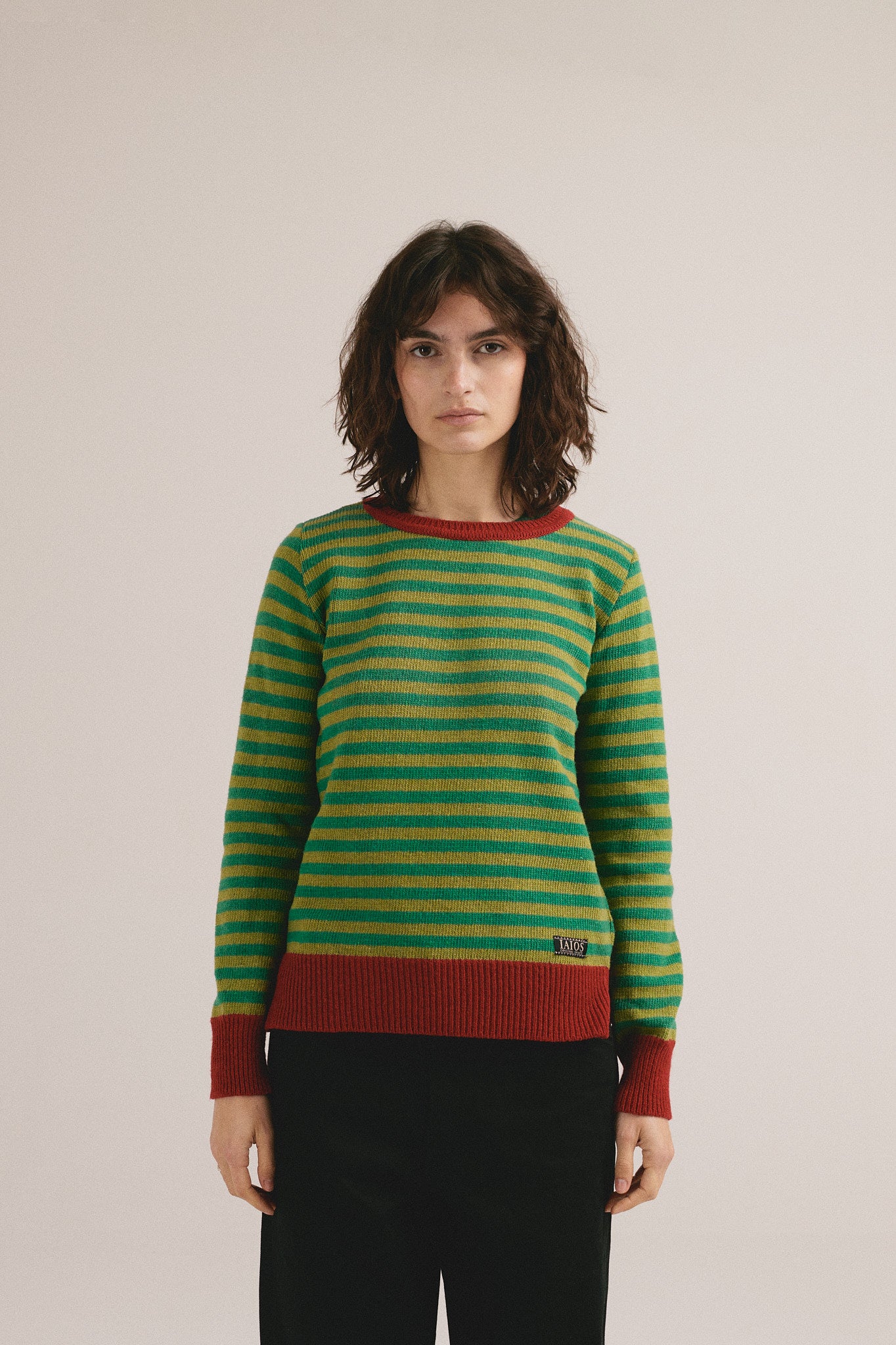 Mujer joven vistiendo jersey de punto a rayas verdes y amarillas con estilo casual moderno.