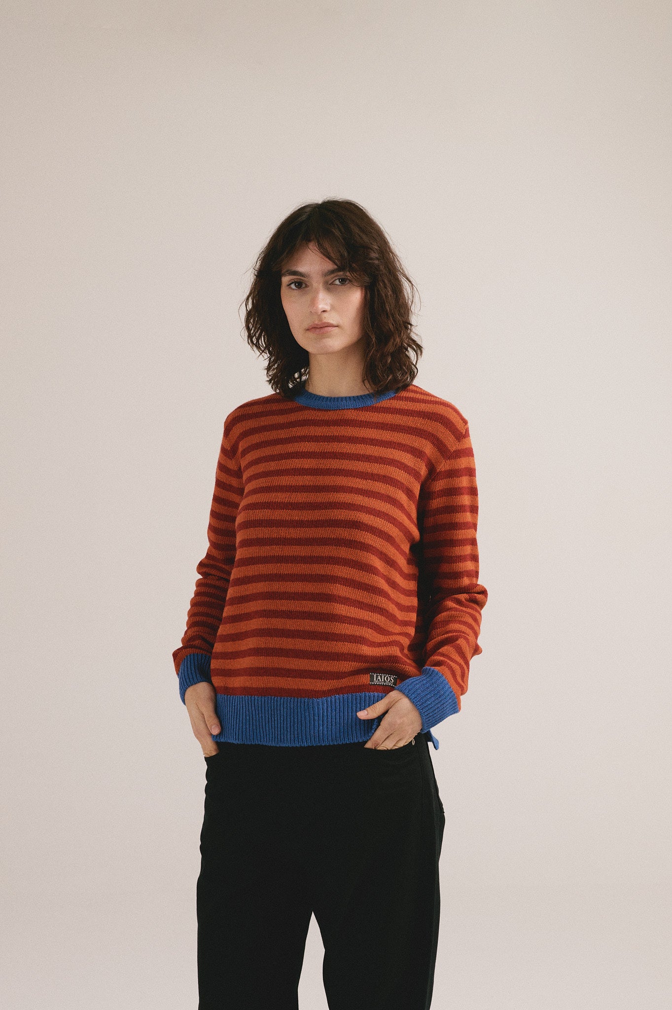 Modelo femenina con suéter de punto de rayas en tonos rojo y naranja con cuello y puños azules de IAIOS.