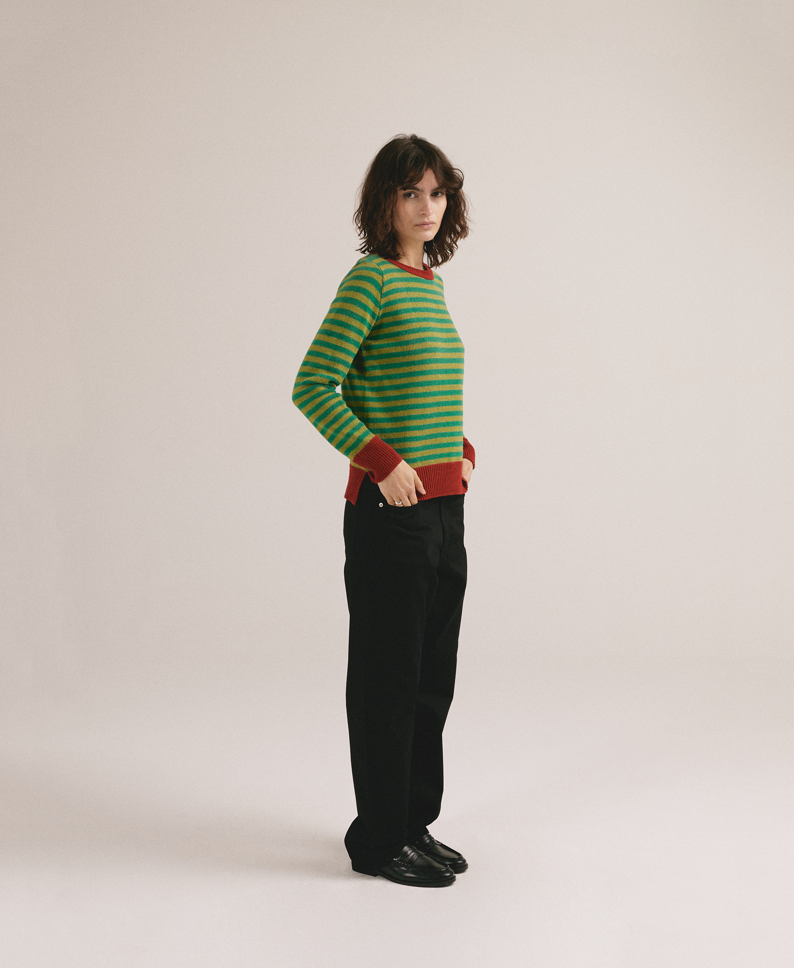 Mujer con jersey de punto a rayas verdes y amarillas con detalles rojos de IAIOS y pantalón oscuro.