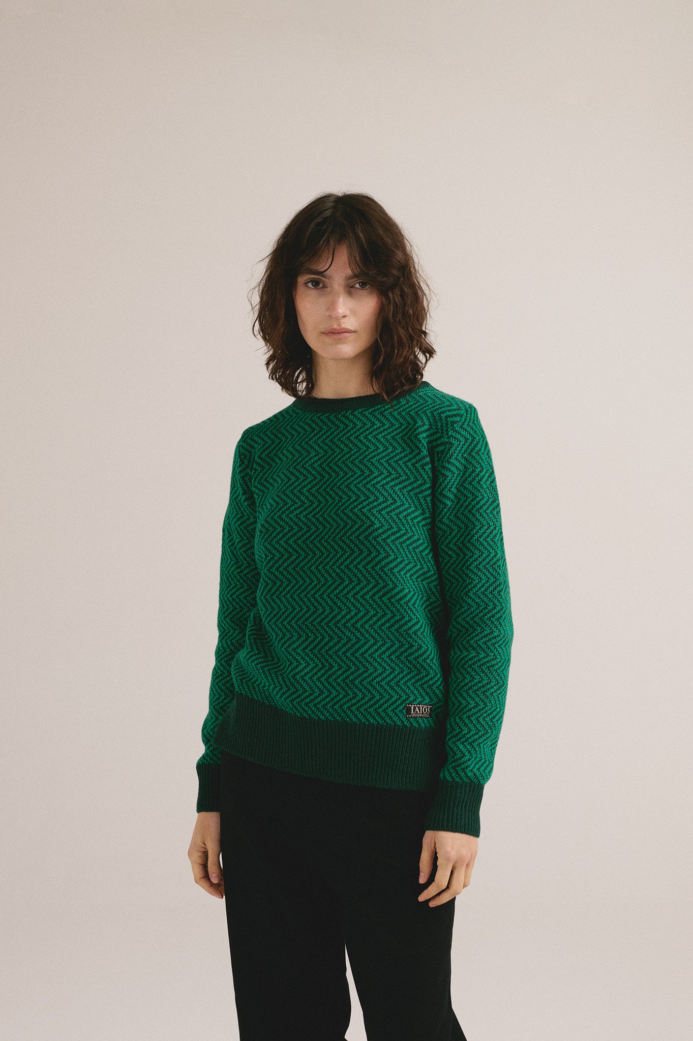 Mujer con jersey de punto verde con estampado geométrico de IAIOS y pantalón oscuro.