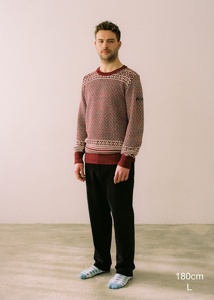 Fotografía de cuerpo entero en la que se detalla la altura (180cm) y la talla del jersey (L). Jersey de hombre IAIOS rojo y blanco con motivos navideños, detalle del tejido, moda sostenible elaborada con hilo reciclado en talleres de Catalunya (España).