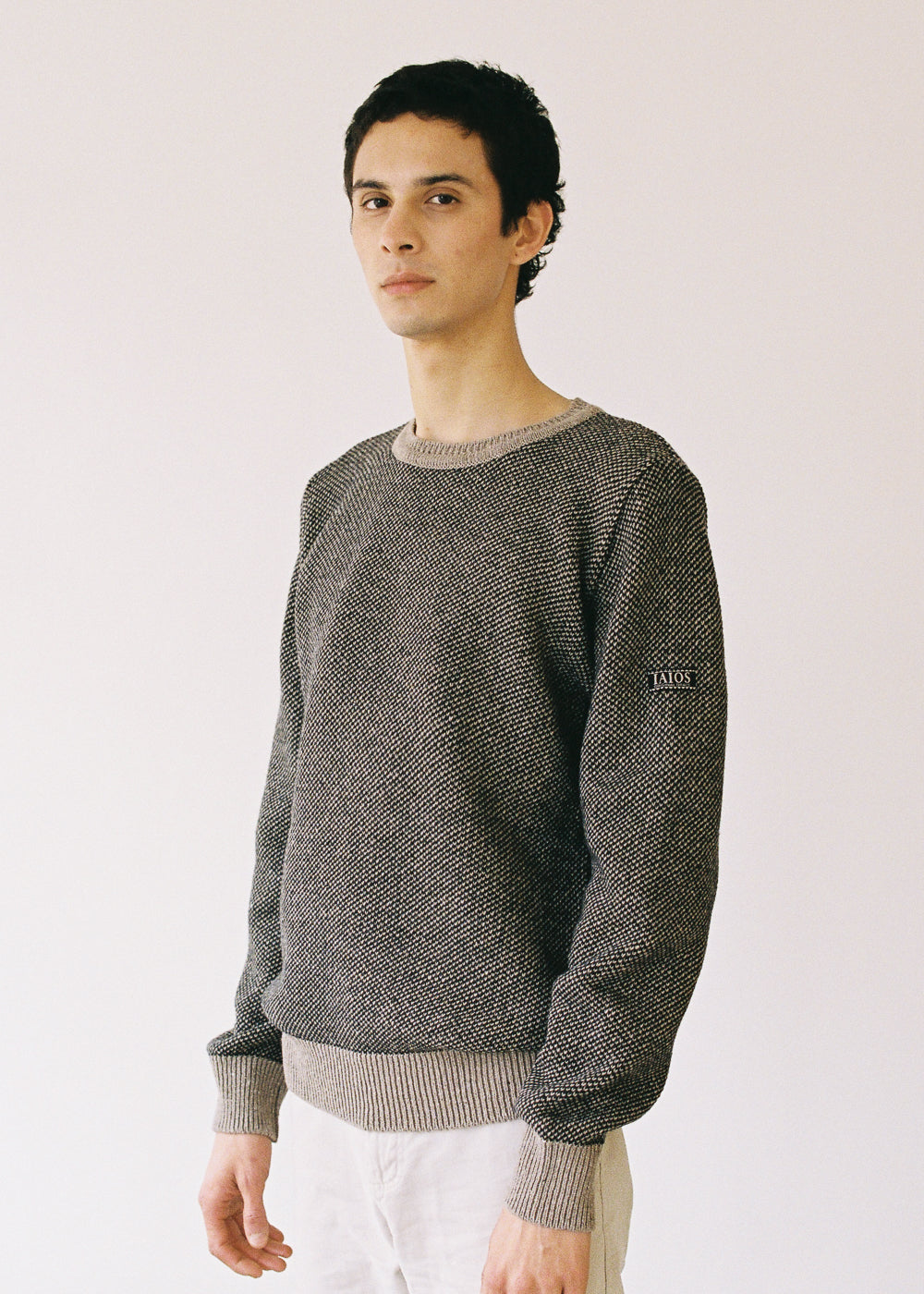 El modelo lleva el jersey unisex IAIOS negro y beige en punto grano de arroz, moda sostenible hecha en Catalunya (España) con hilo reciclado, ideal para invierno.