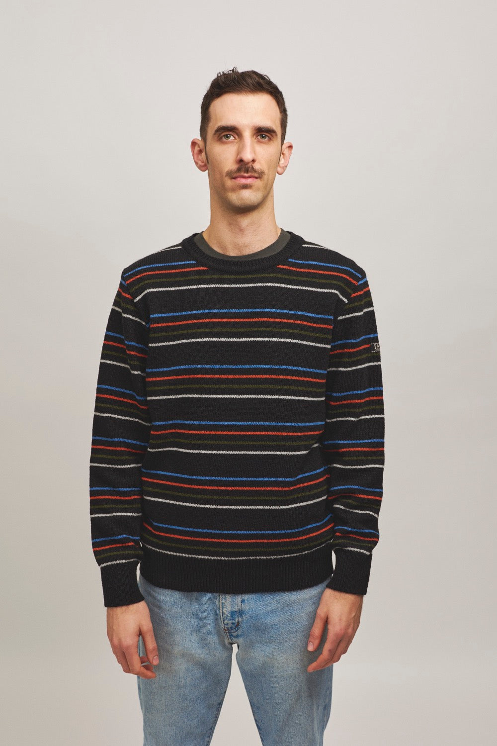 Modelo con jersey unisex negro de punto con rayas finas en tonos vivos, inspirado en jerseys tradicionales, hecho en Catalunya (España) con hilo reciclado.