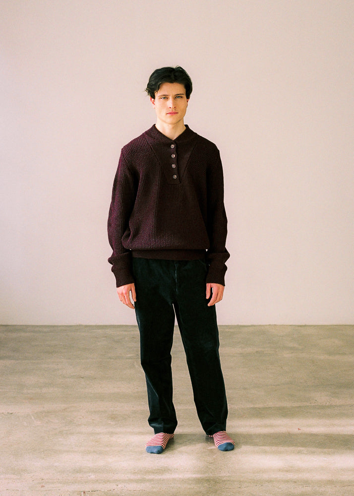 El modelo lleva el jersey unisex IAIOS oversize color granate con botones frontales, tejido de punto reciclado, hecho en Catalunya (España), ideal para un estilo cómodo y atemporal.