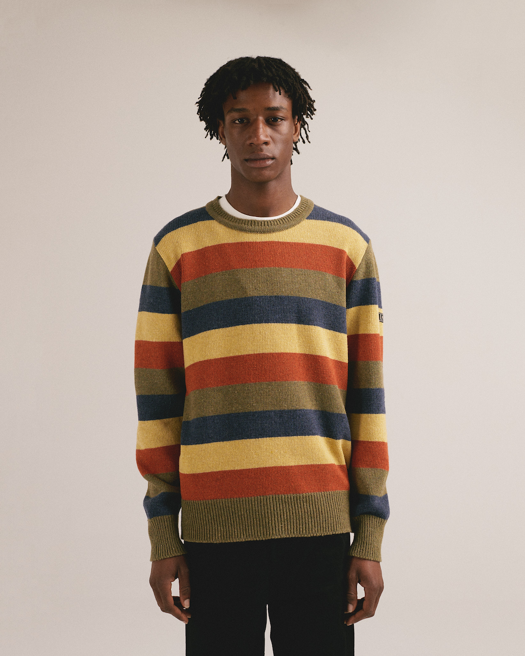 Modelo masculino con suéter de punto de rayas horizontales en colores cálidos y azules de IAIOS.