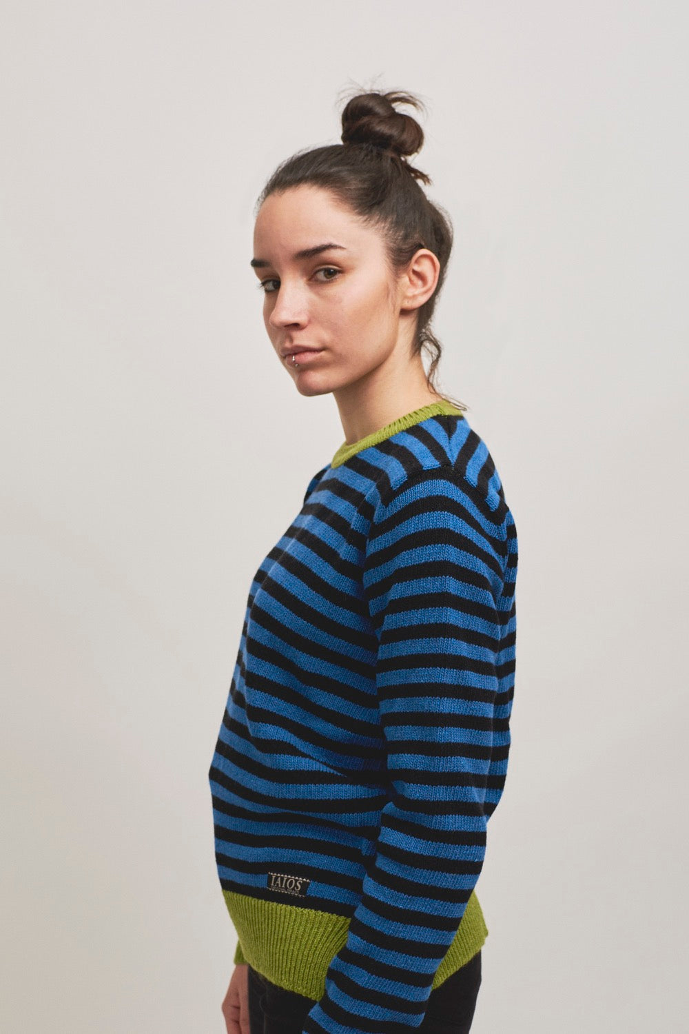 Modelo con jersey Truth unisex de rayas negras y azules con canales en color pistacho, corte recto y aberturas laterales, uno de los más vendidos de IAIOS.