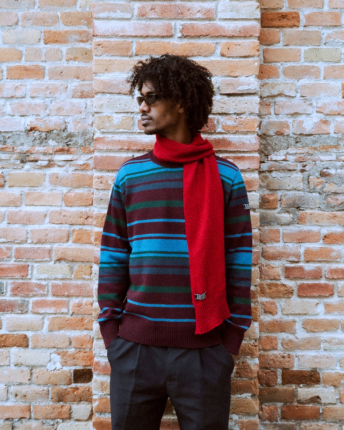 El modelo lleva el jersey unisex IAIOS de rayas en tonos azul, verde y burdeos, con cuello redondo y ajuste regular, hecho en Catalunya (España) con hilo reciclado.