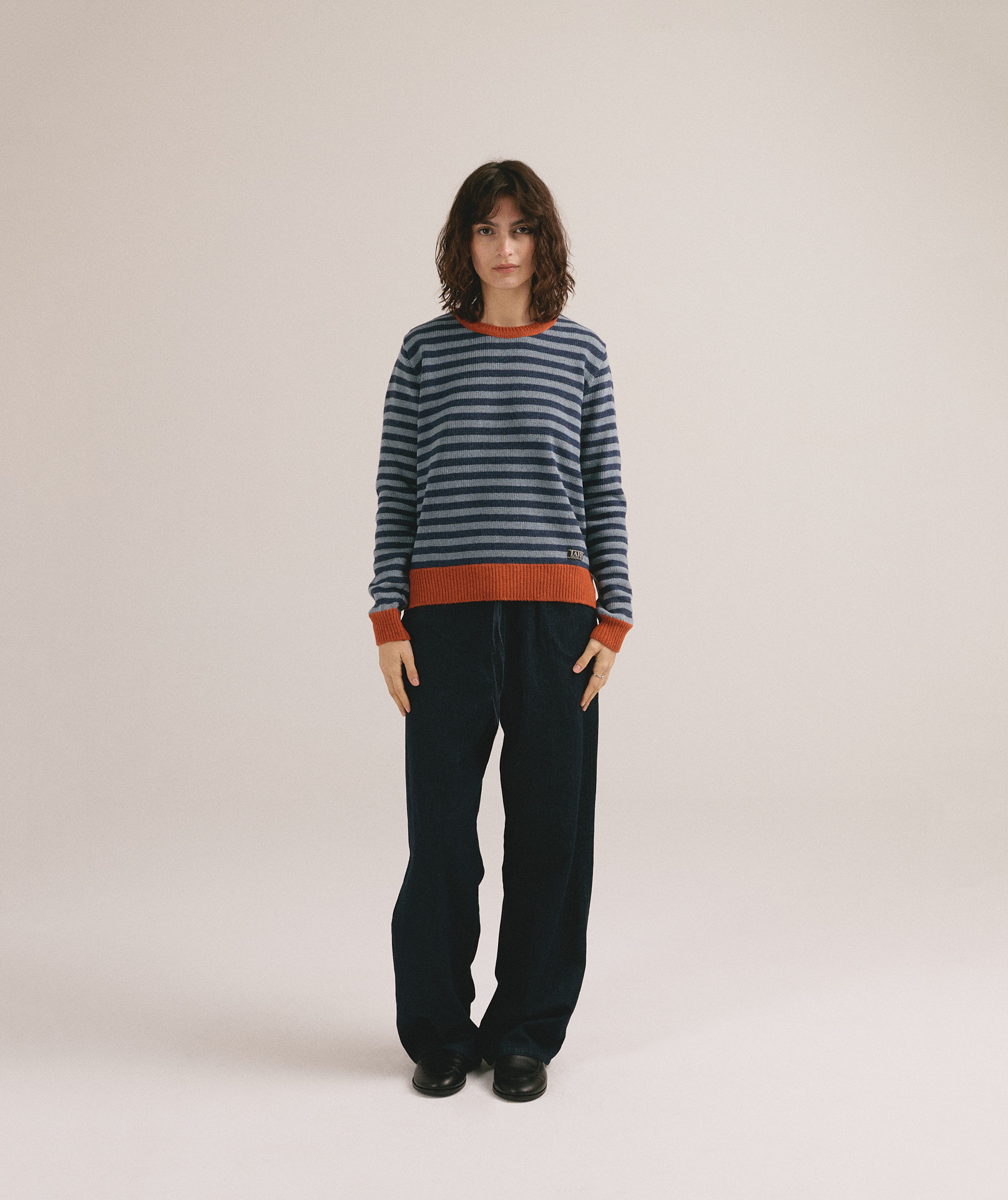 Modelo femenina con suéter de punto de rayas en azul y gris con cuello y puños naranjas de IAIOS.