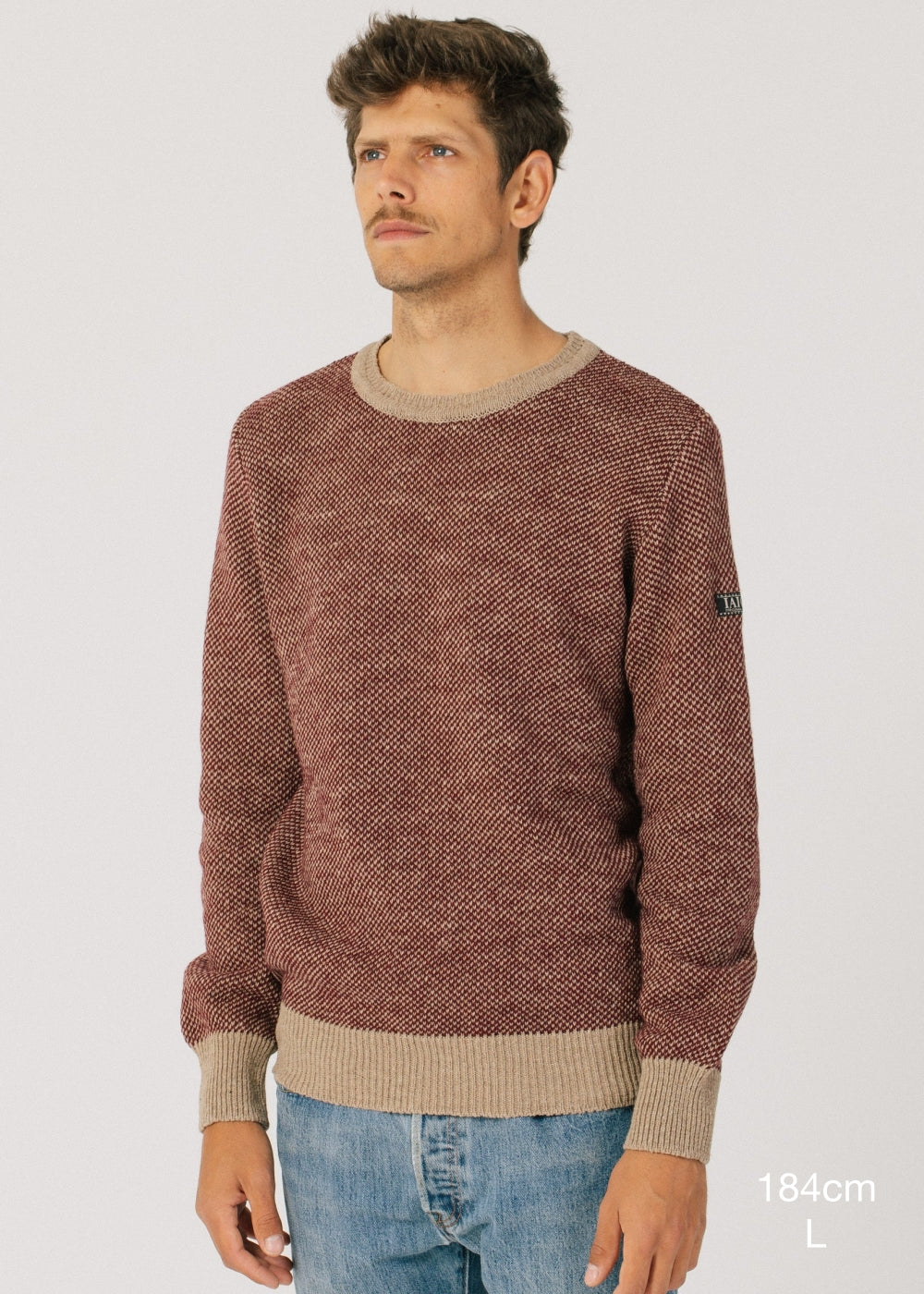 El modelo lleva el jersey IAIOS unisex rojo y camel con textura de punto grano de arroz, moda sostenible elaborada en talleres de Catalunya (España) con hilo reciclado.